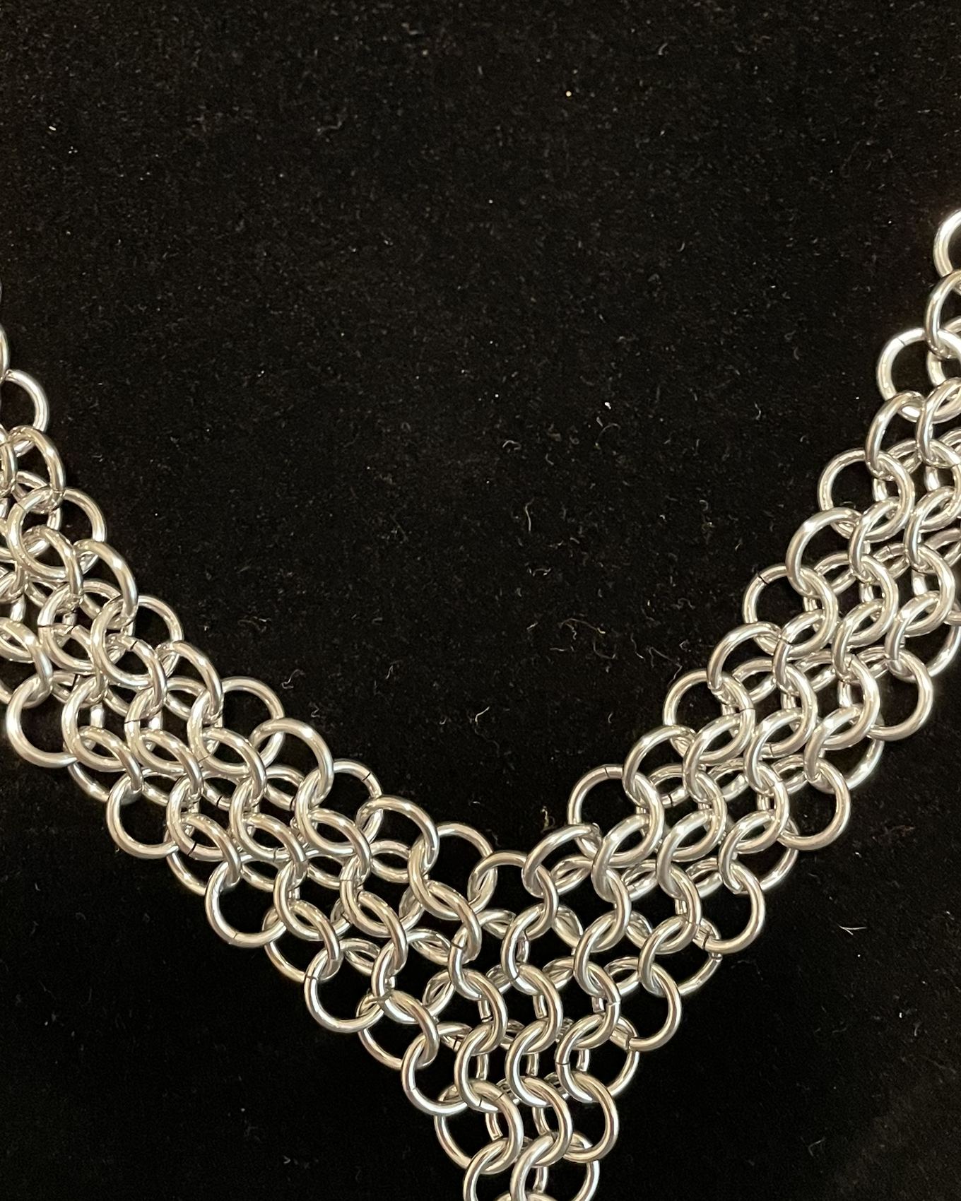 Close-up of a silver chainmaille collar on black velvet, each ring visible