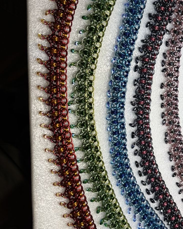 A row of the same chainmaille design woven in copper, green, blue, purple and silver