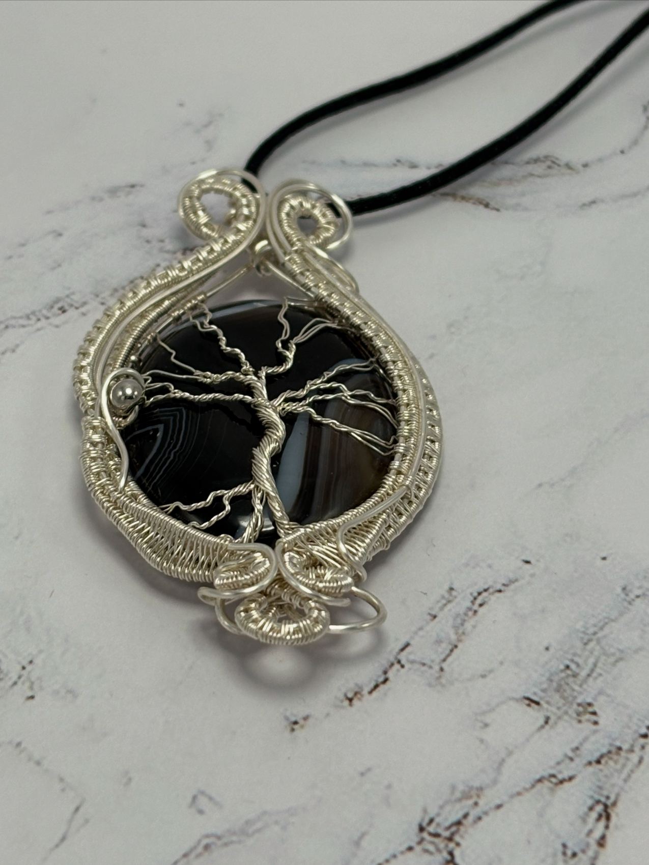 Tree of Life pendant: silver wire woven around a banded black agate, on white marble
